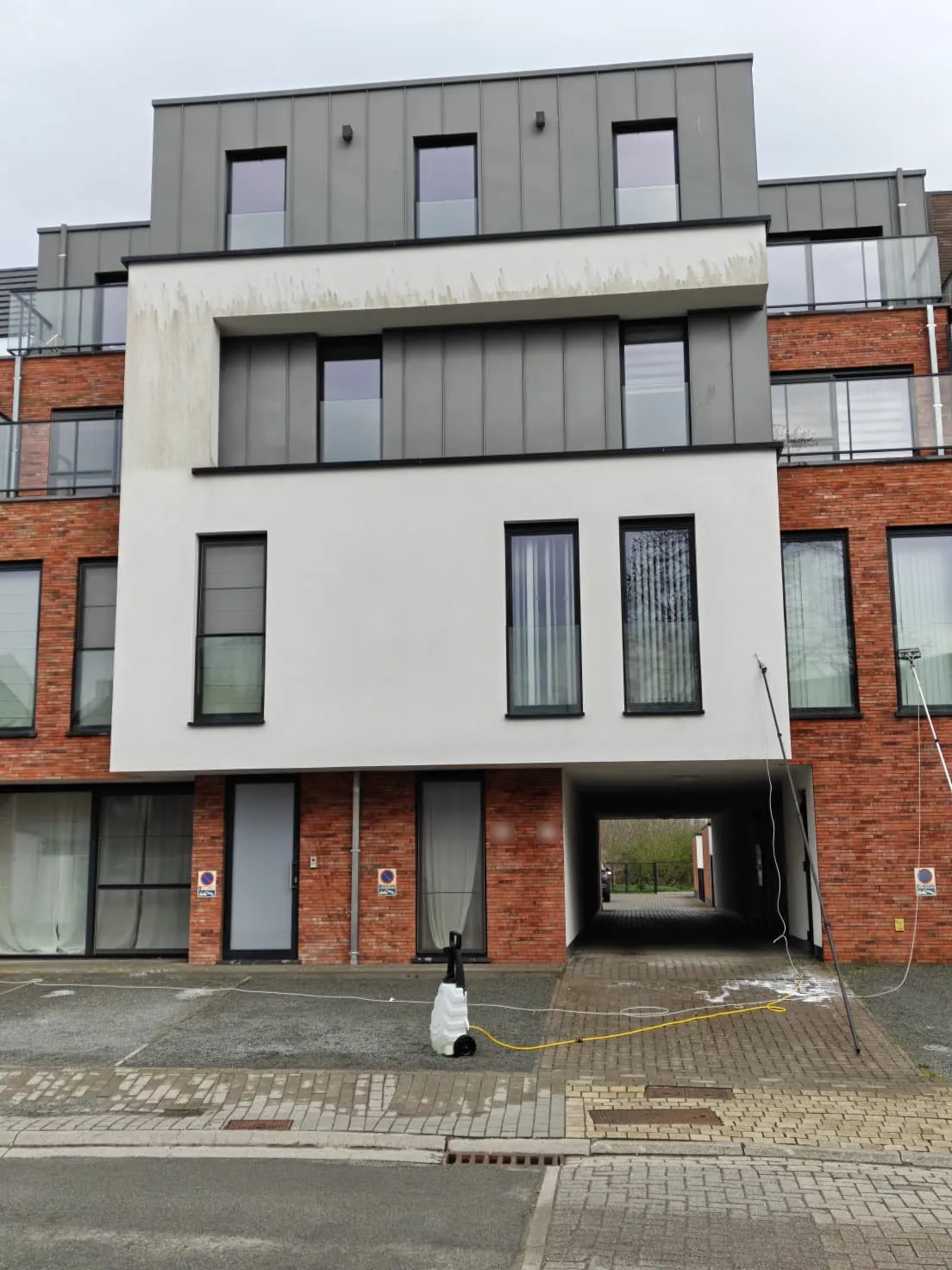 Witte gevel van een appartementsgebouw met groene aanslag, voor de reiniging door ABX Cleaning.